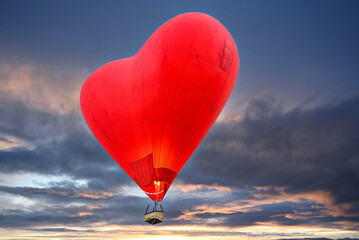 Red heart shaped hot air balloon flying over sunset sky