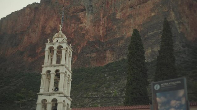 Static upward view of monastery or cathedral bell tower against jagged rocky cliffs in Leonidio Greece