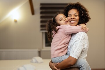 Portrait of happy mother and daughter hugging each other in bedroom at home
