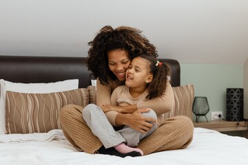 Togetherness Concept. Cheerful african american mother and daughter playing together on bed