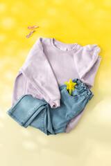 Children's lilac sweater and folded jeans on a yellow background. Stylish children's clothes