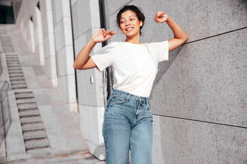 Young beautiful smiling hipster woman in trendy summer white t-shirt and jeans clothes. Carefree woman, posing in the street at sunny day. Positive model outdoors. Cheerful and happy