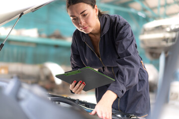 Auto mechanic in uniform service car engine in workshop garage. Skill female repairman using tool repair maintenance vehicle automobile. Young adult technician working examining in transportation shop