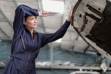Auto mechanic in uniform service car engine in workshop garage. Skill female repairman using tool...