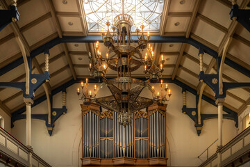 Old candle-lit chandelier against a pipe organ in a church