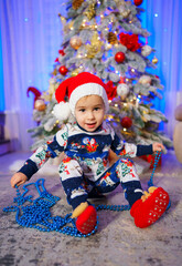 A mesmerizing image capturing an adorable baby adorned with a Santa hat, cheerfully situated in front of a resplendent Christmas tree.