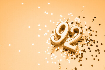 92 years celebration festive background made with golden candles in the form of number Ninety-two lying on sparkles. Universal holiday banner with copy space.