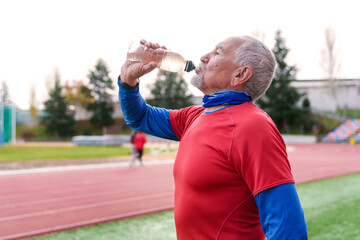 Mature athlete drinking water from a bottle, taking a hydration break on a sports track