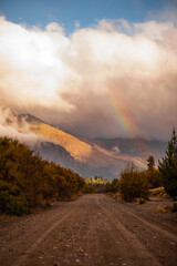 Country road surrounded by lush trees in mountains, with rainbow in the background