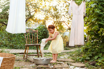Little girl in dress washing clothes in metal basin while helping mom with chores in backyard