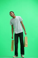 A man in a gray T-shirt, on a green background, full-length, with bags