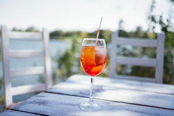 Elegant long-stemmed glass of spritz aperol with slice of orange on white wooden table.