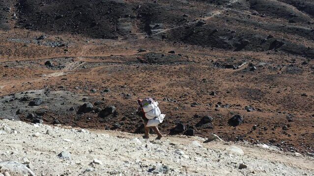 Mountain sherpa porter carries heavy load on back. Carry things and cargo in hard to reach places in Nepal. Working porter for tourists in Himalayas. It hard job. Food delivery to remote settlements