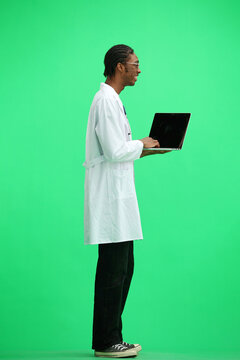 A Male Doctor, On A Green Background, In Full Height, Uses A Laptop