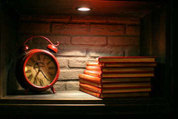 Stylish antique alarm red clock with red books on dark background on modern shelf wall - Powered by Adobe