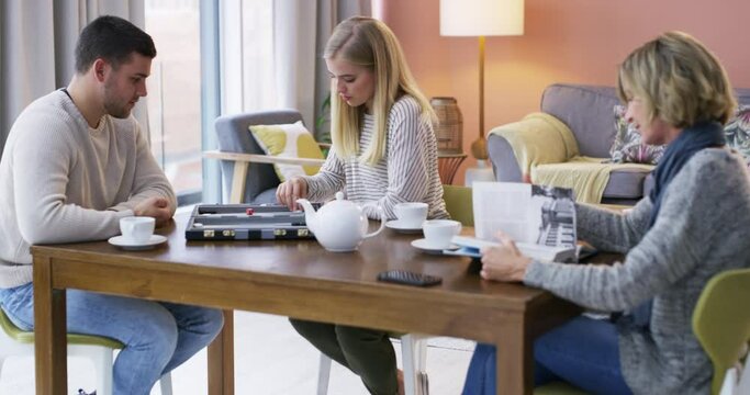 Family, playing and board game in living room for fun, bonding or activity together at home. Young man and woman enjoying competitive match in luck with rolling the dice by mother on table at house
