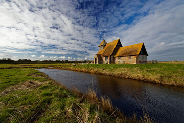 Fototapeta premium St Thomas Becket Church on the marshes in the village of Fairfield on Romney Marsh in Kent England UK surrounded by grazing sheep and water courses.