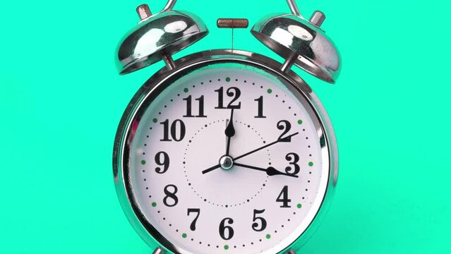 Classic vintage alarm clock isolated on green background. Retro alarm clock running fast. Clock hands move fast, the beginning of time twelve o'clock to one o'clock.