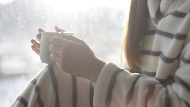 窓際で暖かい飲み物を飲む日本人女性