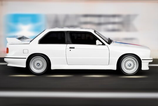 Madrid, Spain; 12-10-2023: Side view of scale model of a white Bmw M3 E30 sports car from the year 1986 running at full speed near ship containers in port