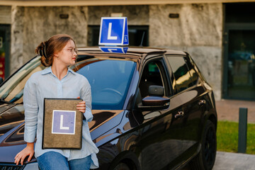 Young charming female driver posing with L Plate on the roof of car. Driving school and people...