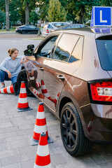 Vertical shot of disappointed girl student driving school sitting near a traffic cone after a...