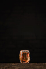 A glass transparent cup of freshly brewed black hot aromatic tea with warm soft light isolated on dark background. Green tea on wooden table on a black brick wall, soft sunlight shone. Space for text.
