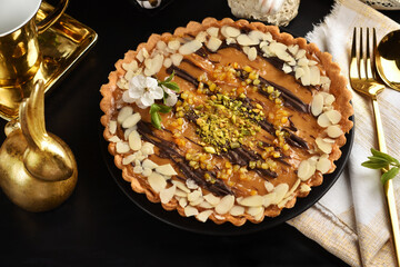 Top view of Easter caramel Mazurek tart on black table with white and golden decors
