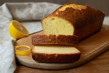 Homemade sliced pound cake with half of lemon on a cutting board on a wooden background.