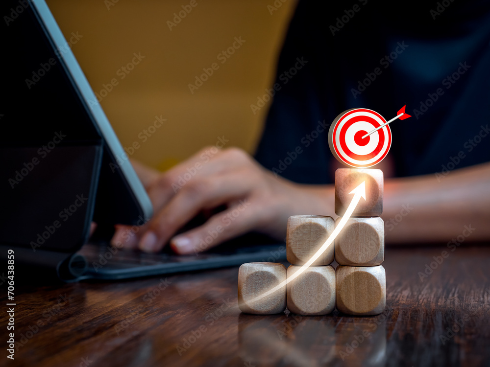Poster 3d target icons and rise arrow on wooden cube blocks as graph steps while businessperson working wit