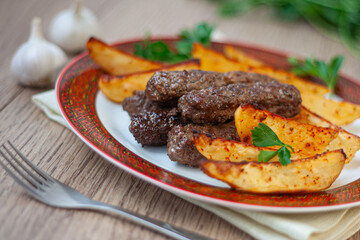 Lula kebabs on a white plate with a red border with baked potatoes and greens.