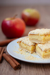 Sliced apple pie made from shortcrust pastry with cottage cheese cream and apple wedges on a white plate on a wooden background.