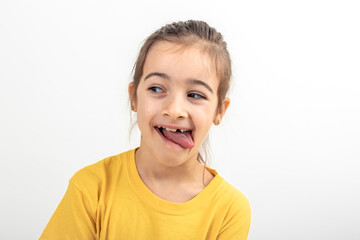 A little girl grimaces with her tongue hanging out on a white background. - obrazy, fototapety, plakaty