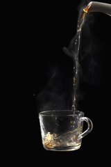 Process brewing tea on black background. Transparent glass cup of freshly brewed black tea steaming...