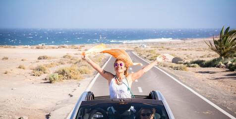 Happy women traveler enjoy road trip with a convertible car. One woman outside the roof have fun....