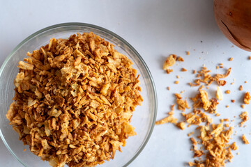 Golden crispy fried onion flakes in a glass dish on a white background. Top view.