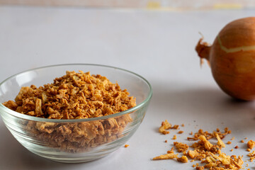 Golden crispy fried onion flakes in a glass dish on a white background.