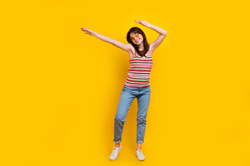 Full body photo of lovely peaceful girl wear striped tank denim trousers dancing raising hands up isolated on yellow color background