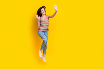 Fototapeta na wymiar Full size photo of cheerful woman dressed knit top jeans jumping making selfie on smartphone say hi isolated on yellow color background