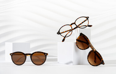 Trendy sunglasses of different design and eyeglasses on podiums on white background. Minimalism....