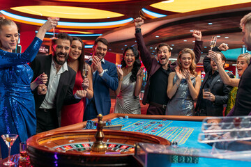 Cheerful Group of Rich Young People Gathered Around a Roulette Table at a Modern Casino. Cinematic...