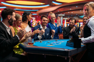 Group of Glamorous People Playing Card at Blackjack Table on a Casino Floor. Crowd Celebrating as a...