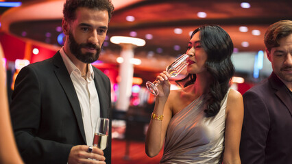 Multiethnic Couple Having a Fun Conversation at a Casino while Drinking Champagne and Gambling at a Roulette Table. Handsome Hispanic Man and Elegant Asian Female Enjoy Nightlife During Their Holiday