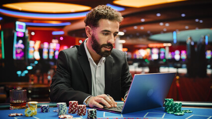Portrait of a Young Man on Casino Floor, Using Laptop Computer to Play Online Casino Betting...