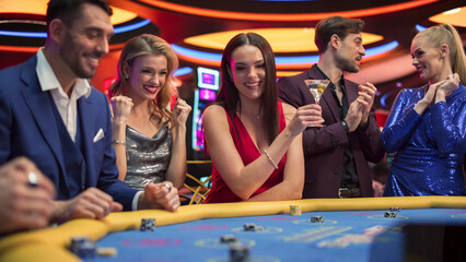 Group of Diverse Young People Gambling at the Baccarat Table in Casino. Glamorous Guests Placing...