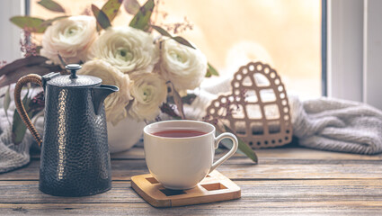 Cozy home composition with a cup of tea, teapot and flowers.