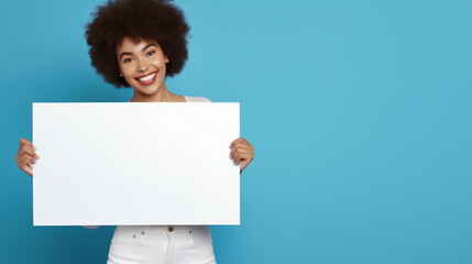 A cheerful young African-American woman with a radiant smile and a voluminous afro hair holds a blank white sign, ready for customization, against a striking blue background