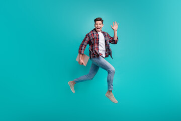 Fototapeta na wymiar Full length photo of excited friendly man dressed plaid shirt jumping walking waving arm holding gadget isolated turquoise color background