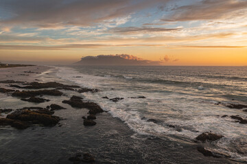 Sunset on the beach with waves breaking over the rocks