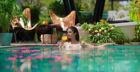 Indian Asian Hindu relax woman bathing rose petals water park pool edge resort hold glass drink...